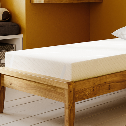 Wooden bed frame with white mattress against a mustard yellow wall.