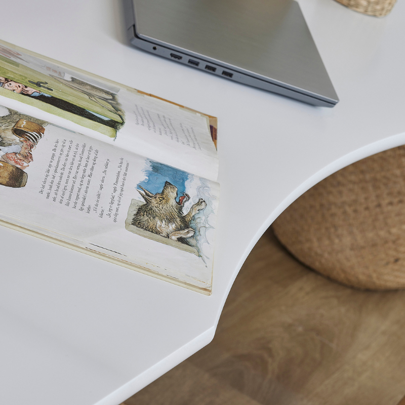 Open book with illustrations on a white loft bed desk surface next to a laptop