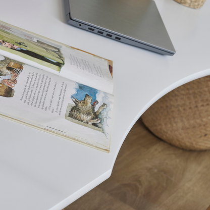 Open book with illustrations on a white loft bed desk surface next to a laptop
