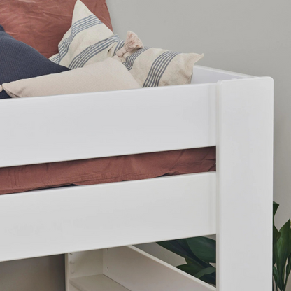 Close-up of white wooden bed corner with colorful cushions on a neutral background